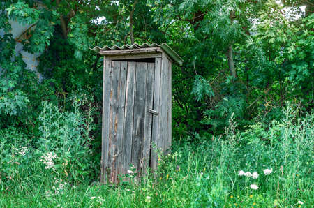 Old wooden toilet on the edge of the forest on the background of green trees in grassの写真素材