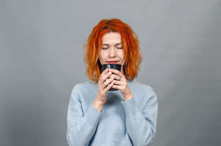 Young red-haired woman with drink with closed eyes from pleasure