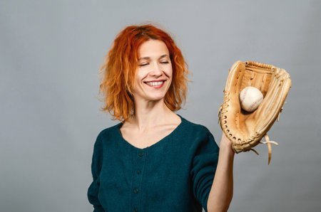 Portrait of slender woman holding big baseball glove in her hand. Smiling, looking at the camera....