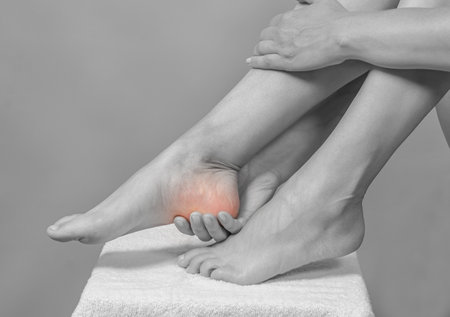 Female hands holding feet. Pain in heel. Feet on white towel.の写真素材