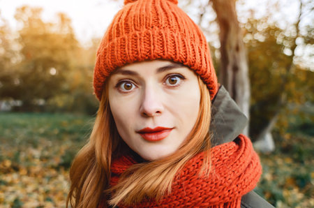 Bright cute young woman in orange warm knitted hat and scarf. Autumn portrait close-up. Blurred...