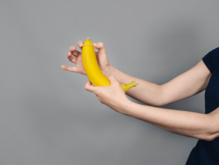 Condom on banana. Female hands put condom on banana. Concept of safe sex.の写真素材