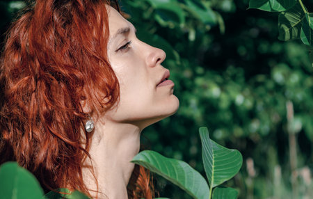 Portrait of a woman in profile against the background of green leavesの写真素材