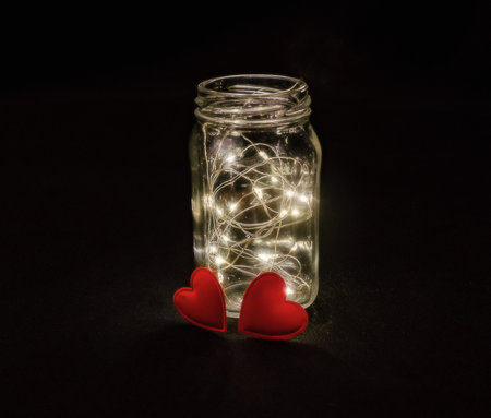 Warmth of two hearts. Atmospheric photo of glowing red hearts in glass. black background
