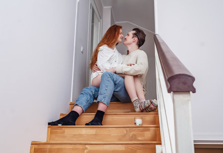 Couple in love hugging on wooden stairs. Red-haired young woman with bare legs in arms of man....