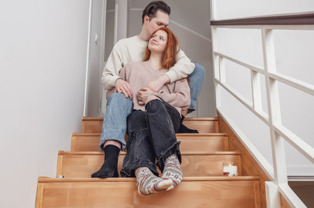 Tender hugs of lovers on wooden stairs. Red-haired young woman in casual clothes in hands of man. Feeling, sensuality.の写真素材