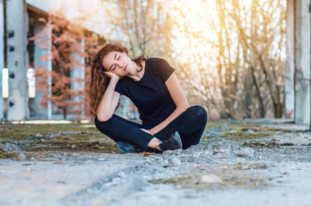 Resting teenage girl sitting on the ground with legs crossed. closed eyes. Sunset background.の写真素材
