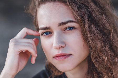 Attractive face of young woman with wavy hair. Blue eyes, black eyebrows, smile.の写真素材