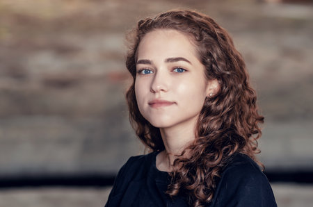 Nice girl, portrait in pastel colors on background of old painted wall. Perfect smile on face, curly hair. close-up.の写真素材