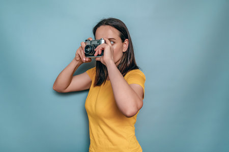 A woman takes pictures with an old film camera. Yellow boot cap, black hair, blue backgroundの写真素材