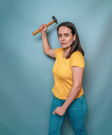 Woman holds in her hands and swings hammer at viewer. Female anger