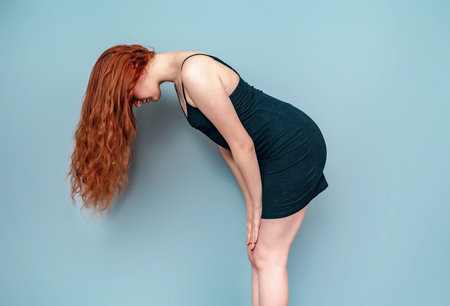 Side view of woman standing, leaning forward. Black short dress, long red hair.の写真素材