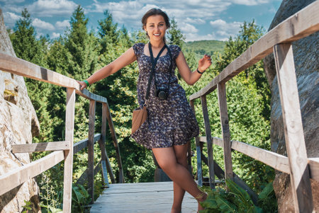A beautiful girl in a dress stands on a wooden bridge against the background of the forest