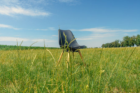 Black chair on field of green grass in summer. One chair as a symbol of loneliness.の写真素材
