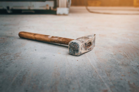 An old hammer with a wooden handle lies on a concrete floor