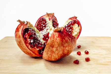 Cut pomegranate with ripe red juicy seeds on wooden board. Fruit for healthy eating.の写真素材