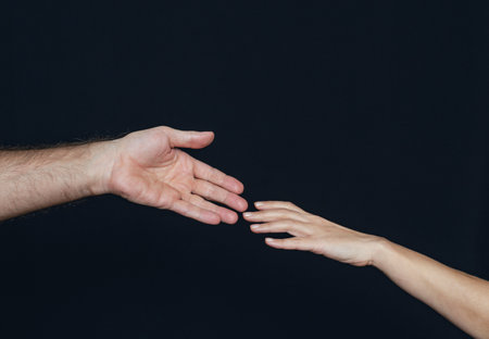 Man's and a woman's hand are reaching towards each other on a black backgroundの写真素材
