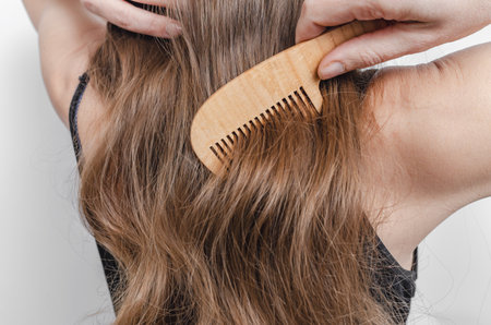 Close-up of wooden comb in woman's hand combing shiny hair. Hair care and hygiene. Gray background