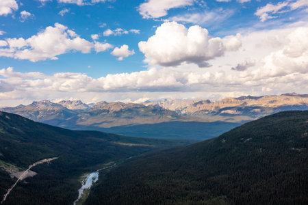 High mountain peaks covered snow and forest below. Cumulus clouds, blue sky. Mountain landscapeの写真素材