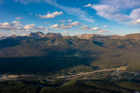 Drone view high peaks with snow under clouds sky. Forest and river below. Mountain landscape Canadaの写真素材