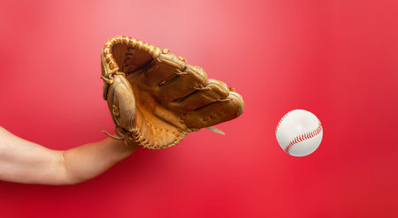 Female baseball gloved hand catches ball. Red background. Active sport, championship, victoryの写真素材