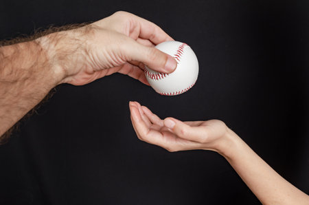 Man hand throws a baseball into a woman hand on a black backgroundの写真素材