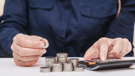 woman in dark clothes stacks coins, calculates profits on a calculatorの写真素材