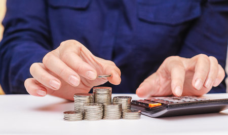 woman in dark clothes stacks coins, calculates profits on a calculatorの写真素材
