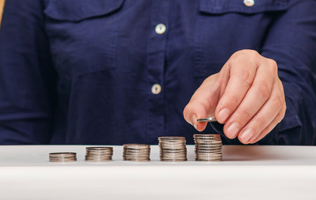 Woman stacks coins on a white table, dark clothes