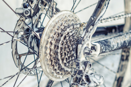 Enlarged bicycle wheel at car wash. Spokes, chain. Washing bicycle with jet of foam. Maintenanceの写真素材