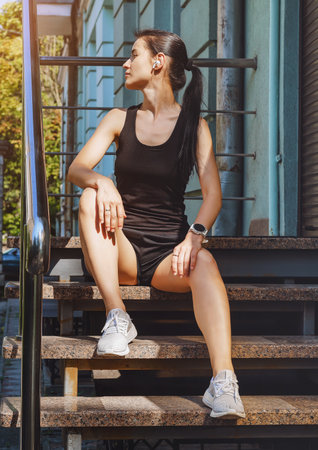 Woman in sports clothes sitting on steps and listening to music on headphones.の写真素材