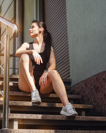 Woman in sports clothes sitting on steps and listening to music on headphones.の写真素材