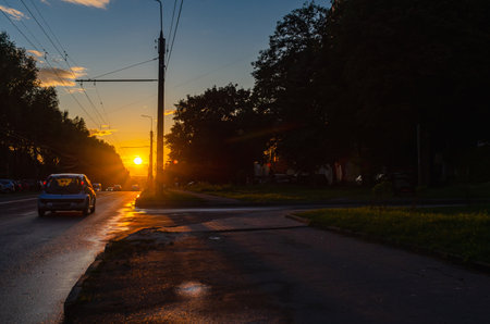 Asphalt road in city with sunset. Number of cars parked along the road. Lanterns and trees. Duskの写真素材