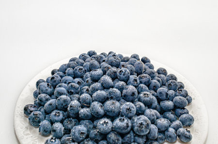 Side view of blueberries on white plate, white background. Drops of water on blueberries.の写真素材