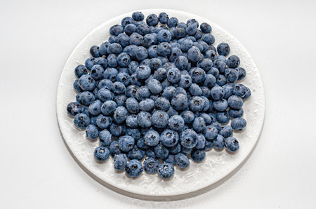 Purple blueberries on white plate, white backdrop. Drops of water on ripe blueberries. Organic foodの写真素材
