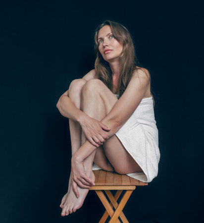 Relaxed Woman with Long Hair Wrapped in Towel, Sitting on Chair in Cozyの写真素材