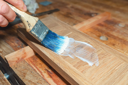 carpenter applies glue to the surface of a board with a brush in a carpentry workshopの写真素材
