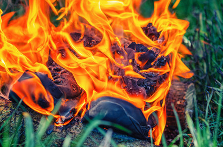 Burning sneakers on green grass, fiery orange flames engulfing running shoes as they blaze in open fieldの写真素材