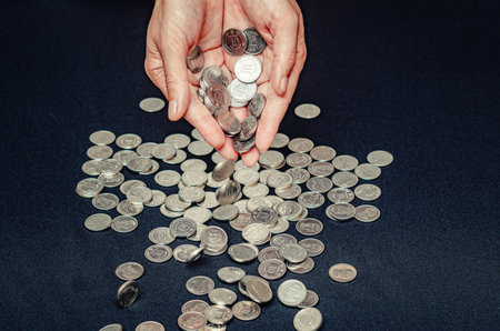 Coins fall from palms into pile. Black background. Concept of economic crisis, global recession, inflationの写真素材