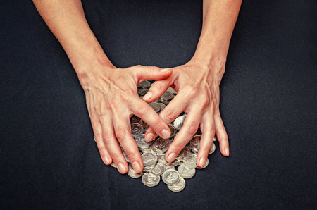 Hands cover heaps of silver coins. Close up concept of theft, misappropriation, fraud and greedの写真素材