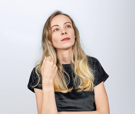 Portrait of dreamy blonde woman with long hair in black top. Hand near her hair. White backgroundの写真素材