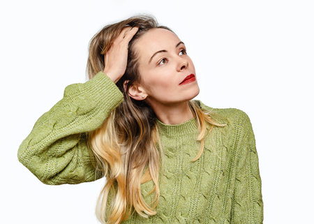 Young woman in green sweater is gracefully posing, Her hand holding strand of hairの写真素材
