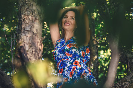 Mature smiling woman with long brown hair on tree in the sun glare. Bottom view. Nature vacationの写真素材