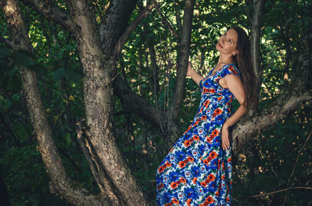 Adult lady on tree enjoying green nature. Forest around her. Concept of women and healthy natural lifestyleの写真素材
