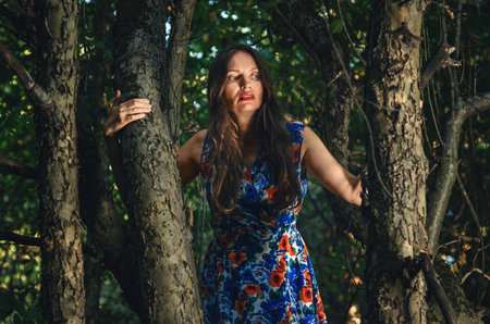 Woman in long colorful dress with long hair like witch between trees in dark forest. Mystical moodの写真素材