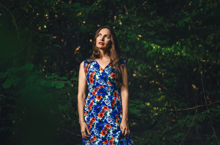 Woman in long colorful dress on path in dark forest. Summer day. Selective focus, blurred mystical moodの写真素材
