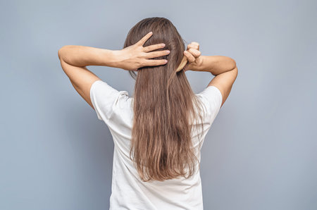Combing long hair. Woman in white t-shirt. Hands behind head. Rear view on gray background isolatedの写真素材
