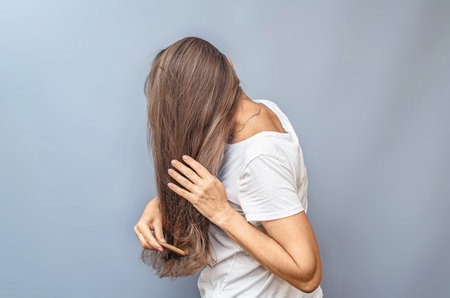 Side view of combining long hair. Woman in white t-shirt. Gray background, isolated. Hair care problemの写真素材