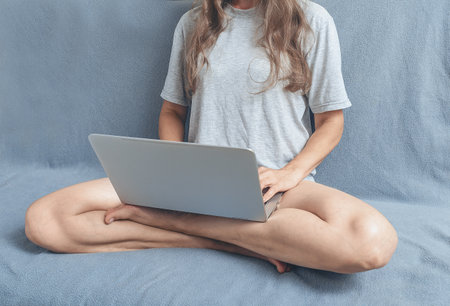 Woman working with laptop at home. Long hair, bare legs, gray t-shirt. Concept of remote work. Cosinessの写真素材