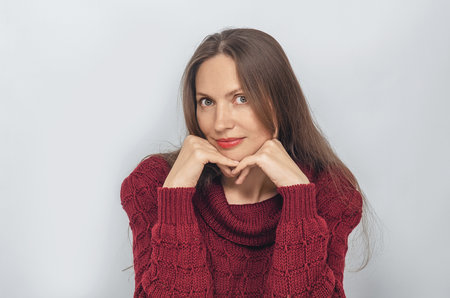 Portrait of woman, wearing a red knitted sweater. Hands under chin, long hairの写真素材